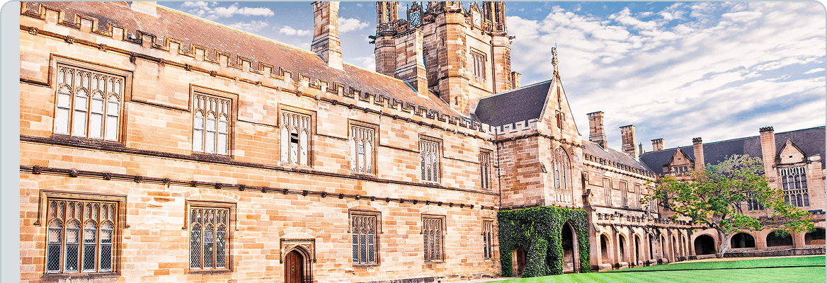 Gothic sandstone university building with a clock tower, arched windows, ivy-covered walls, green lawn, and a partly cloudy blue sky.